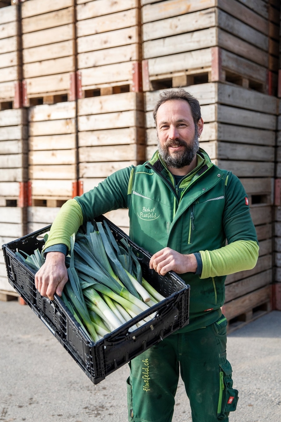 Bauer Michael Reichmuth vom Biohof Fluofeld trägt frisches Gemüse vor Holzkisten