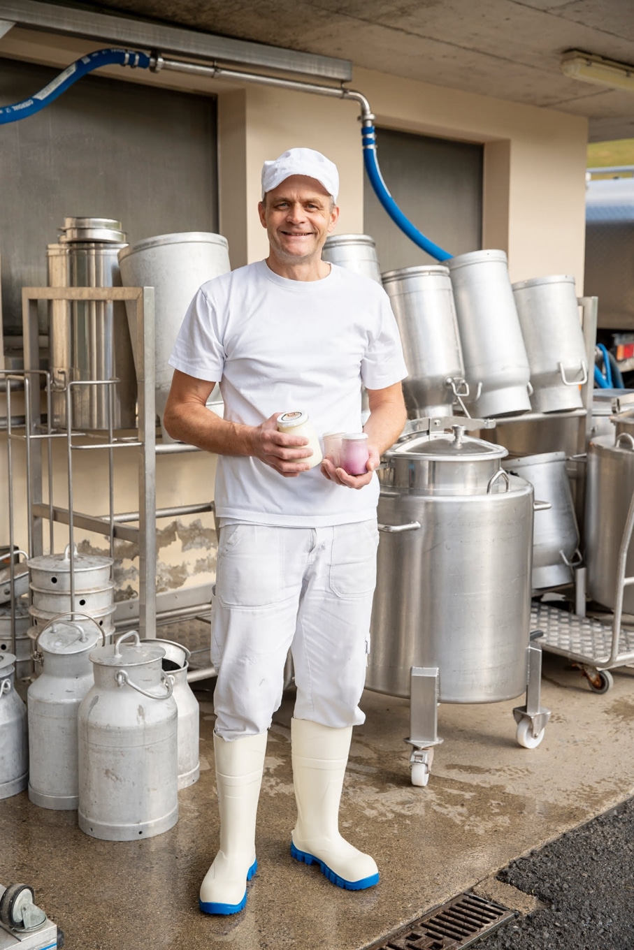 André Rust-Meuwly von der Chäs-Hütte Rust mit Milchkanne und Joghurt im Molkereibereich