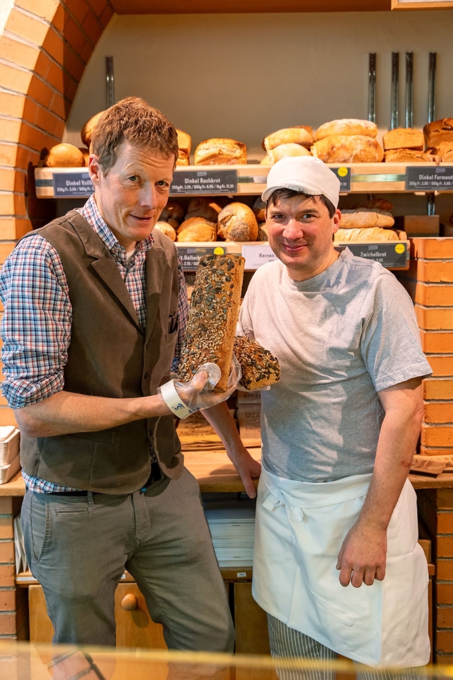 Beat Philipp (l.) und ein Bäcker präsentieren Brot in der Bäckerei Vier Linden